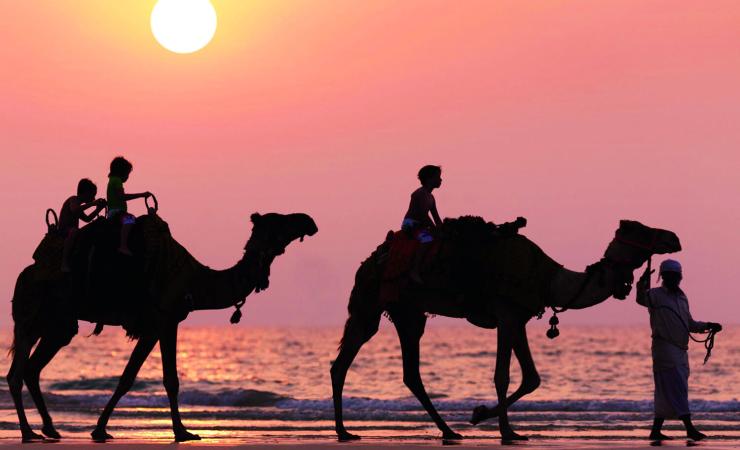 Deti na ťavách na pláži pri západe slnka pri The Ritz-Carlton, Dubai, Jumeirah Beach