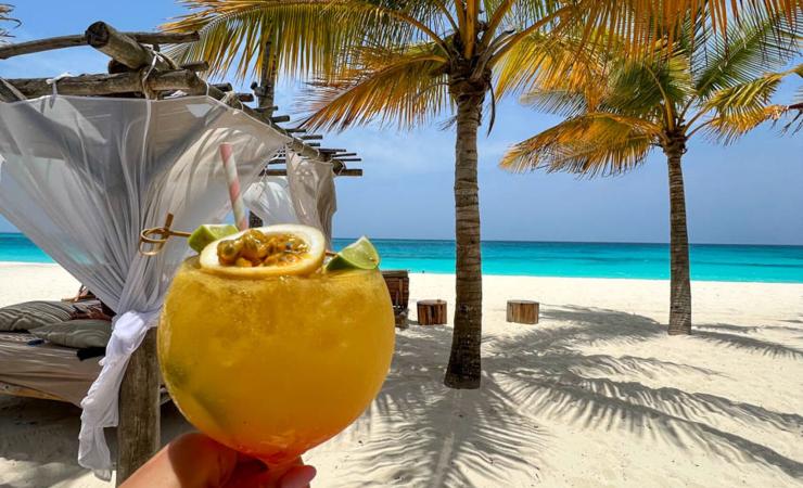 Exotický žltý nápoj s ovocím na bielej pieskovej pláži na Zanzibare.